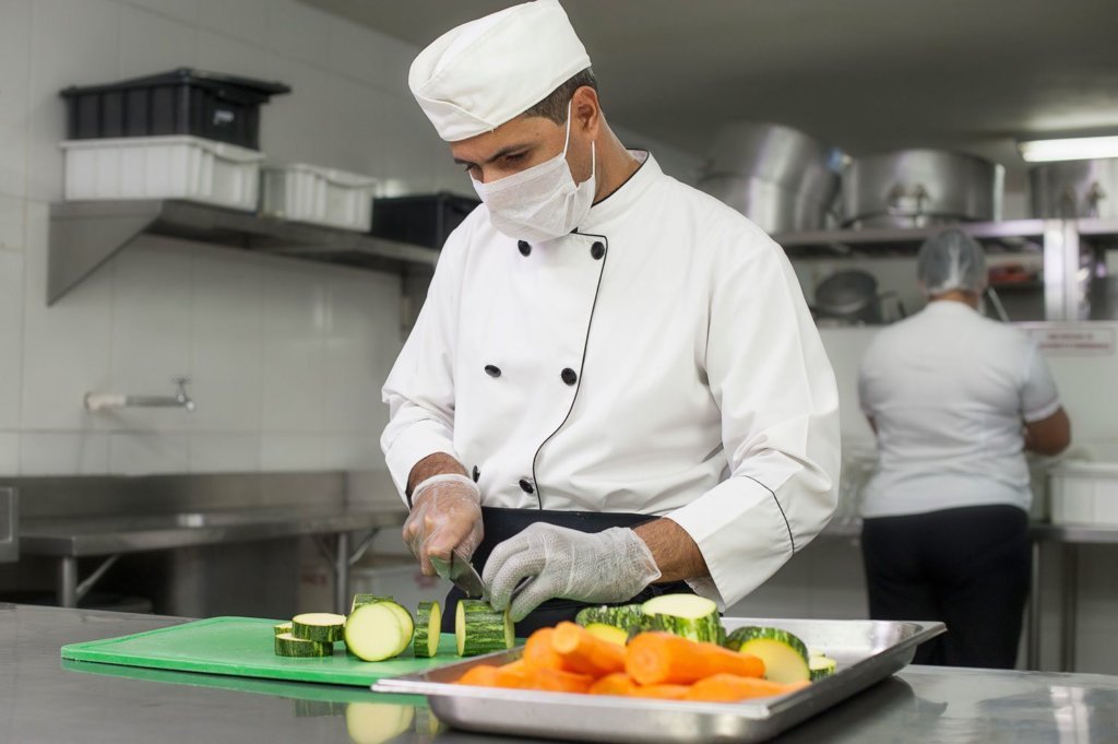 Chef utilizando touca e máscara em uma cozinha industrial para preparar alimentos com segurança